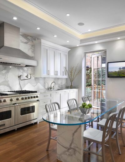 Modern kitchen interior with stainless steel appliances, white cabinetry, marble backsplash, and a glass dining table.