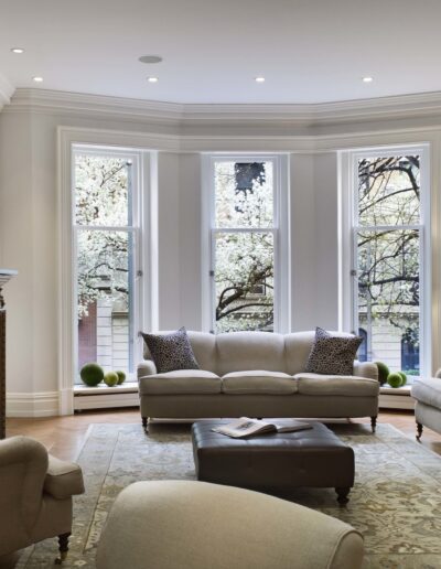 Elegant living room with neutral tones, classical design elements, and a view of trees through large windows.