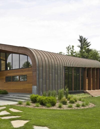 Modern curved architecture home with wooden facade surrounded by greenery.