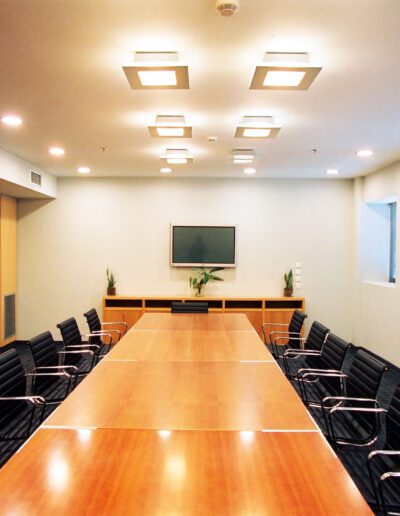 Modern conference room with a long table, black chairs, and a mounted television on the wall.