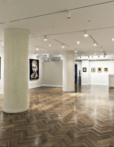 Art gallery interior showcasing various framed artworks on white walls with wooden flooring and lighting fixtures.