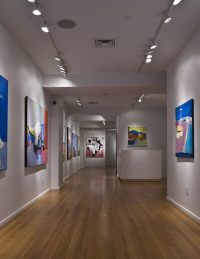 Interior of an art gallery exhibiting colorful abstract paintings on white walls with track lighting.