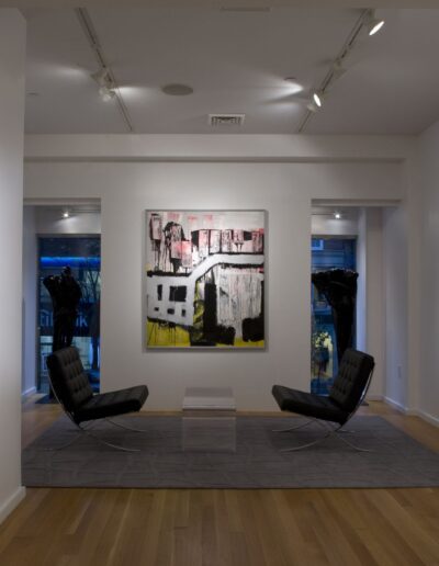 Modern art gallery interior with varied paintings on white walls and seating for viewers.