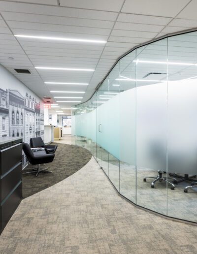 Modern office interior with curved glass partition walls and meeting area.