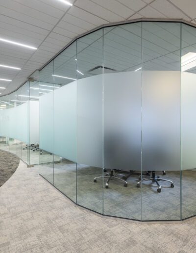 Modern office with glass walls and a curved design, featuring a meeting area with chairs and a table.